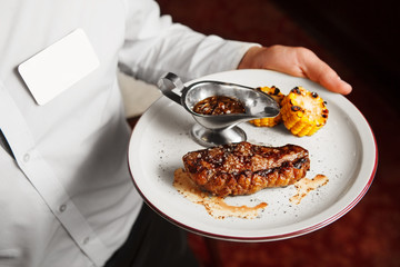 Waiter serve on plate beefsteak with grilled corn and sauce
