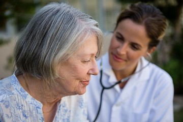 Obraz premium Female doctor examining senior woman with stethoscope in park