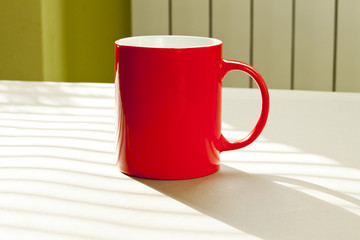Red mug standing on a table against wall as a background.