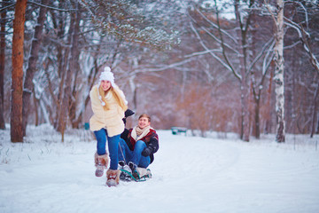 Fototapeta na wymiar A happy couple is riding a sled in the snow in a park in the winter. St. Valentine's Day.