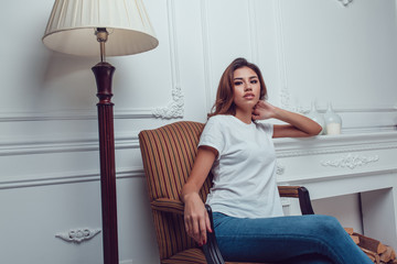 Attractive girl in a white t-shirt sits on a chair. Mock-up.