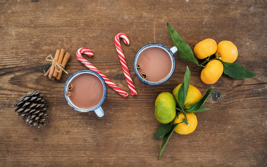 Christmas or New Year attributes. Fresh mandarins with leaves, cinnamon sticks, pine cone, hot chocolate in mugs and candy canes over rustic wooden background, top view