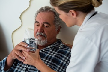 Side view of female doctor giving water to senior patient