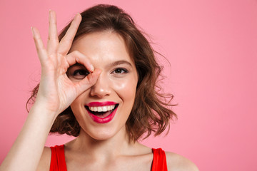 Close-up portrait of young happy girl with red lips looking at camera through OK sign