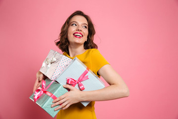 Cheerful young woman in yellow dress holding heap of presents