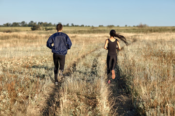 Back view of running woman and man training in field, jogging