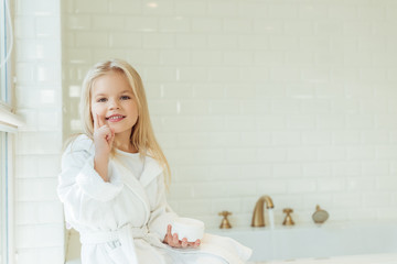 child in bathrobe applying face cream