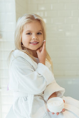 child in bathrobe applying face cream