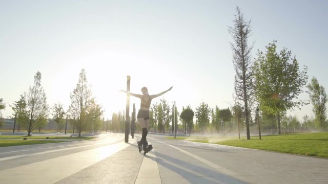 beautiful young woman on rollerblading in the park at sunrise against the background of the rising sun