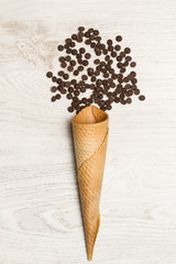 Cono de helado con gotas de chocolate sobre fondo de madera blanca. Vista superior