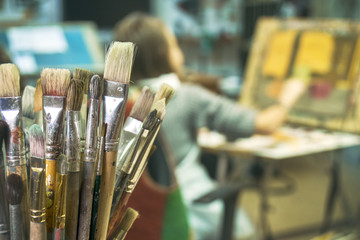 Paintbrushes on the foreground close up and a girl painting a picture on the blurred background....