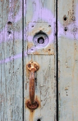 old rusted iron door handle on a green painted wooden door with cracks and missing nails