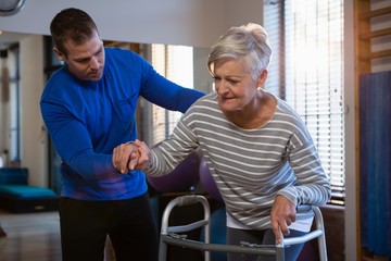 Fototapeta premium Physiotherapist assisting patient to walk with walking frame