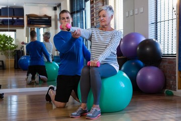Physiotherapist assisting senior woman on exercise ball and
