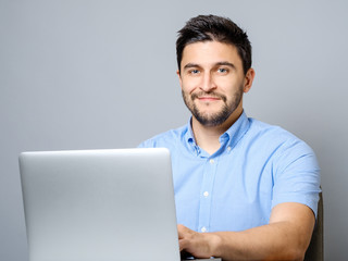 Portrait of young smiling man sitting at the desk with laptop