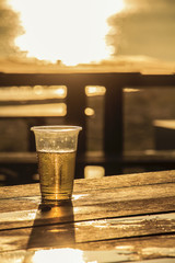 plastic glass which has beer inside on wooden table near beach