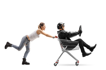 Female punker pushing a shopping cart with a biker riding inside and holding a steering wheel