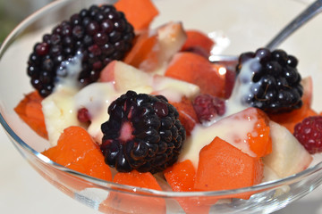 Fruit salad with apricot, peach, raspberry and blackberry  in glass. Perfect dessert with fresh berries and vanilla cream. Closeup.