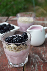 Overnight oats with blackberry yogurt. Delicious breakfast in glass cups on old wooden table, outdoor background,