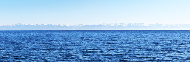 Naklejka na ściany i meble Panoramic view of Lake Baikal and snow-covered mountains on the opposite east coast. Water background