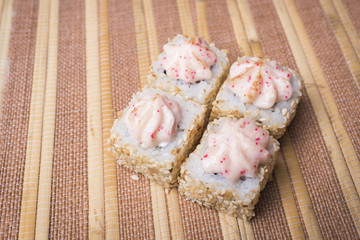 Sushi rolls with sesame and sauce on a brown wooden background