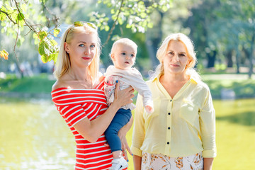 A happy family of three generations, mother, daughter, grandmother and little baby granddaughter, are standing together on the bridge of the river