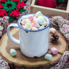 Homemade hot chocolate topped with marshmallow in enamel mug,stay on wooden log, warm scarf on...