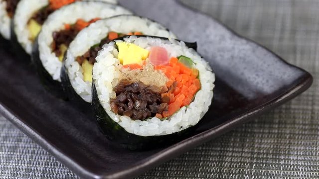 Piece of korean dish Gimbap or Kimbap with tuna and vegetables taken from ceramic plate with chopsticks