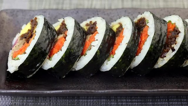 Korean dish Gimbap or Kimbap with tuna and vegetables served in bite size slices on a dark ceramic plate