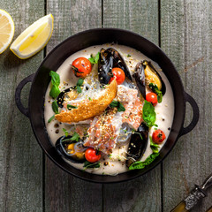 Delicious Asian meal made of sea bass fish, mussels, crab meat and other seafood with tomato and rice noodles on a rustic wooden table. Top view.