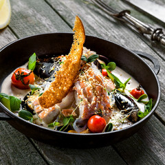 Sea bass fish fillet with mussels, crab meat and cockles with vegetables, cream sauce and rice noodles. Healthy Asian seafood meal on a table.
