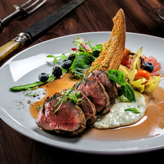 Delicious medium rare meat steak with sauce and salad on a plate. Healthy food made of meat fillet and fresh herbs on a wooden table.