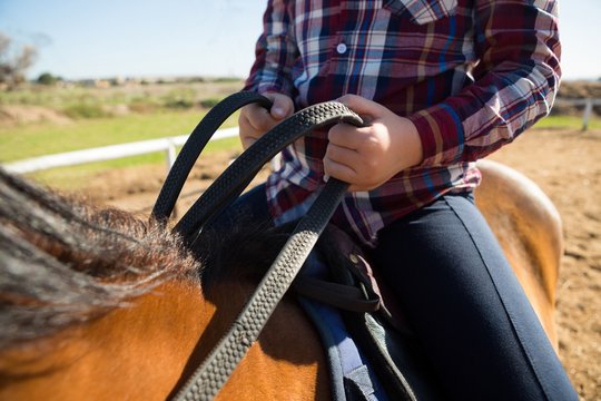 Mid section of girl riding a horse in the ranch