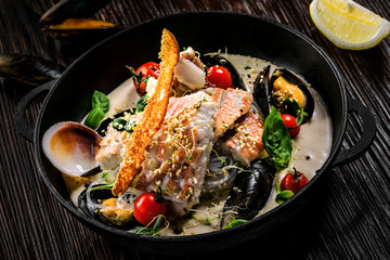 Gourmet Asian meal mad of seafood such as sea bass fish, mussels, crab meat and cockles with vegetables and rice noodles on a table.