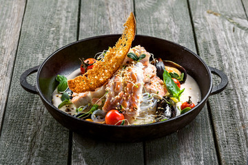 Bowl of delicious seafood meal with rice noodles. Meal made of sea bass fish, mussels, crab meat and other seafood with vegetables on a table.