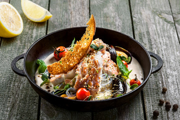 Seafood and rice noodles in cream sauce. Healthy meal made of sea bass fish, mussels, crab meat and other seafood with tomato and rice noodles.