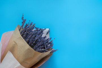 A bouquet of dry lavender in kraft paper on a blue background, symbolizing summer and France. Flat lay, top view.