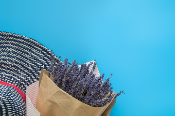 A bouquet of dry lavender in kraft paper on a blue background with a hat, symbolizing summer and France. Flat lay, top view.