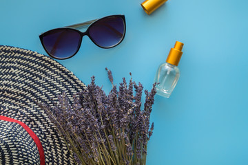 A bouquet of dry lavender in kraft paper on a blue background with a bottle of perfume, sunglasses and a hat, symbolizing summer and France. Flat lay, top view.