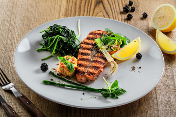 Plate with delicious grilled salmon fish steak and salad on a wooden table. Healthy gourmet food made of fish and vegetables.