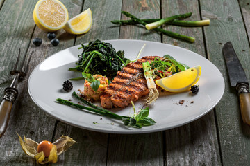 Salmon fish stake cooked on a grill with healthy salad on a plate. Healthy food made of fish and vegetables on a table.