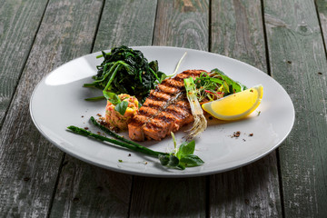 Plate with delicious grilled salmon fish steak and salad on a wooden table. Healthy gourmet food made of fish and vegetables.