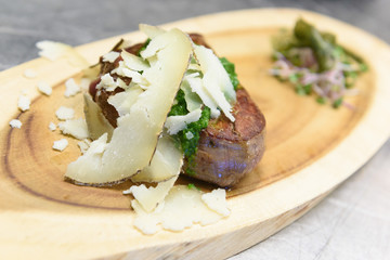 A meat fillet decorated with green pesto sauce and cheese shavings (pecorino nero) on a board made with a tree trunk portion accompanied by salad and green algae