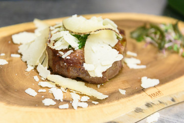 A meat fillet decorated with green pesto sauce and cheese shavings (pecorino nero) on a board made with a tree trunk portion accompanied by salad and green algae