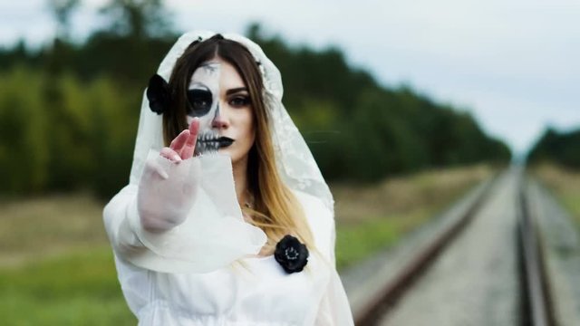 The portrait of young woman with spooky make-up for Halloween in a white bride dress. 4K