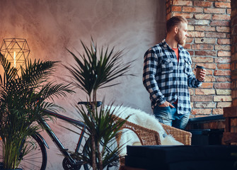 The full body image of blond hipster male drinks coffee.