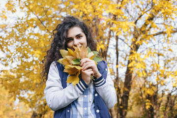 Girl standing in autumn park and holding in hands bunch of leaves. Young woman looking at camera and smile. Outdoor. Close up. Autumn.