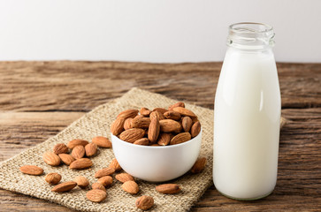 Peeled almonds with bowl and Bottle of almond milk on rustic wooden