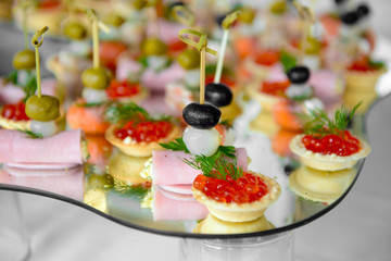Tartlets with red caviar and canapes with meat rolls on the mirror table. Luxurious finger food. Snacks for the party.