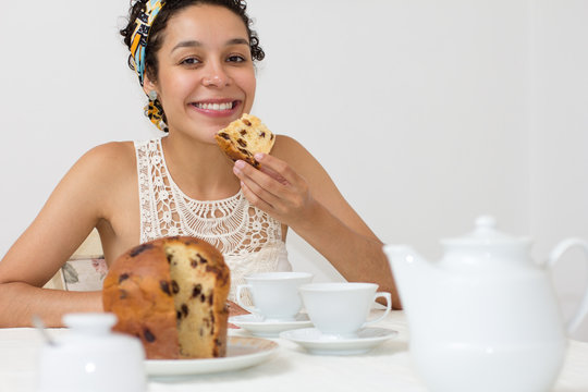 Black Woman Is Eating Panettone. Sitting At A Table With White Utensils..